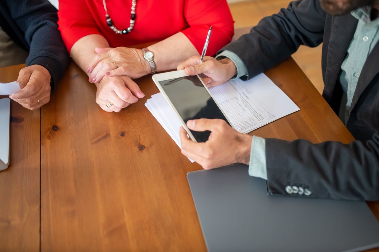 heros-img Business meeting at a wooden table with consultant reviewing documents and using a digital tablet.