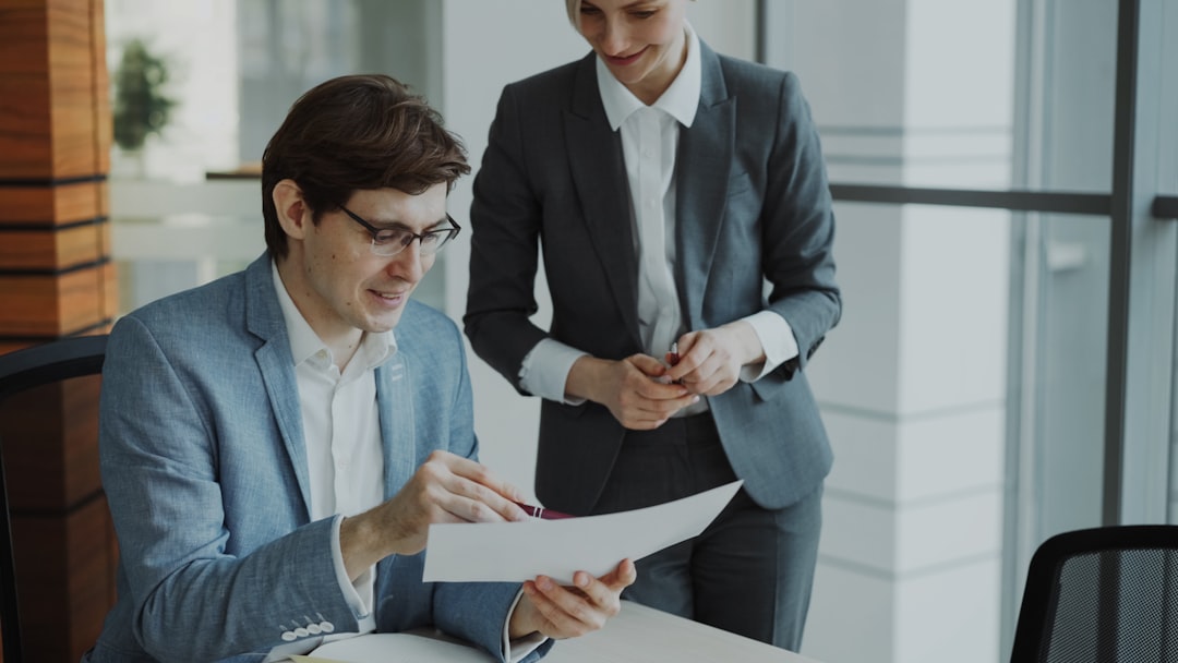 our-story Two business colleagues discussing reports in modern office indoors. Businessman sitting at the table talking his female partner